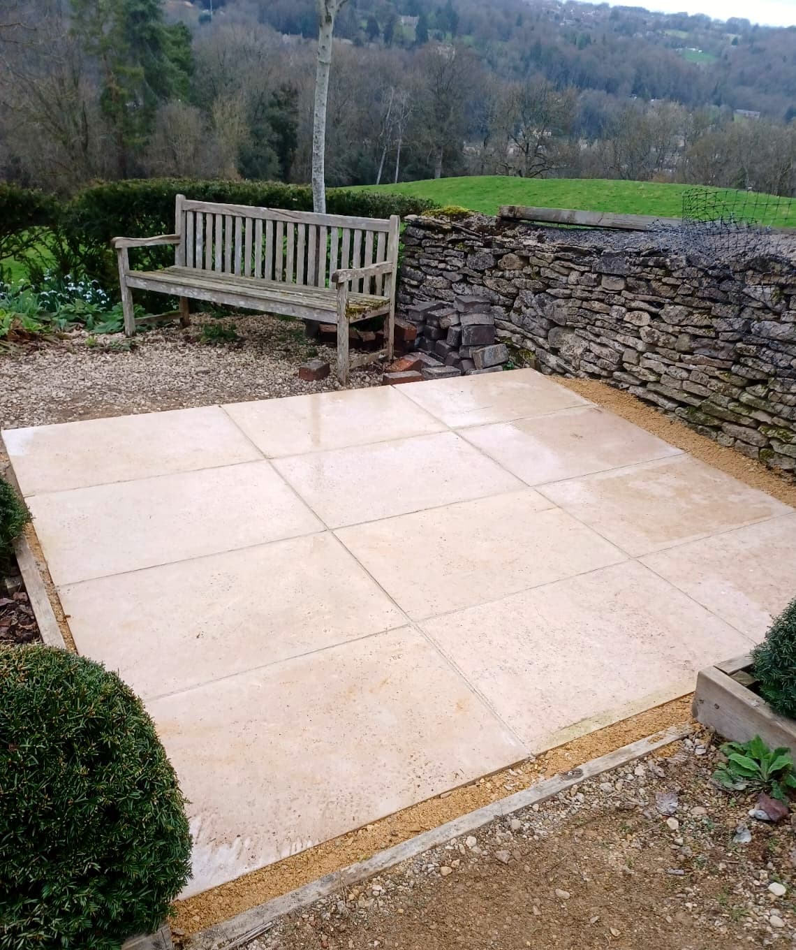 Raised stone patio with wooden bench overlooking hills
